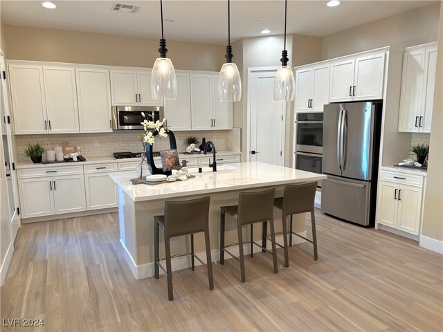 kitchen with an island with sink, pendant lighting, decorative backsplash, white cabinets, and appliances with stainless steel finishes