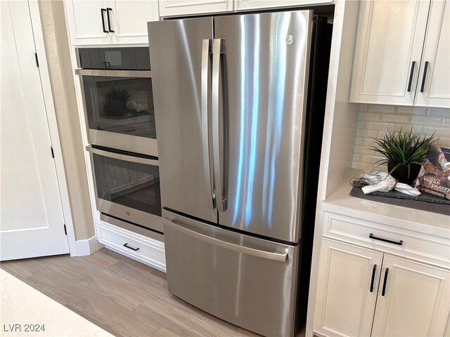 kitchen featuring light stone countertops, appliances with stainless steel finishes, light wood-type flooring, backsplash, and white cabinetry