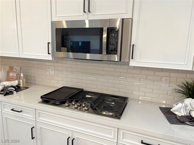 kitchen featuring decorative backsplash, white cabinets, light stone counters, and appliances with stainless steel finishes