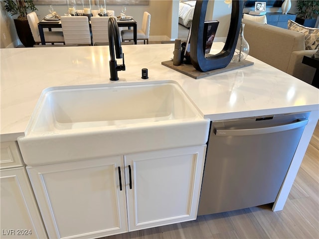 interior details with light stone countertops, stainless steel dishwasher, sink, white cabinets, and hardwood / wood-style floors