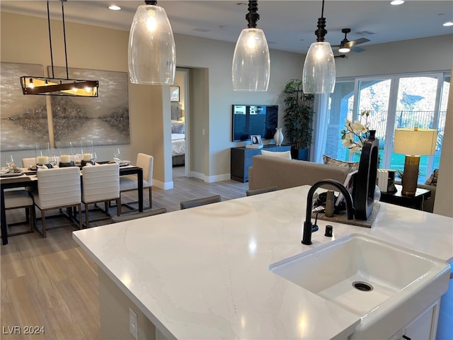 kitchen featuring light stone countertops, a kitchen island with sink, decorative light fixtures, and light hardwood / wood-style floors