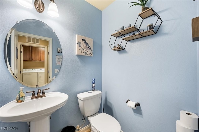 bathroom with washer and dryer, toilet, and sink