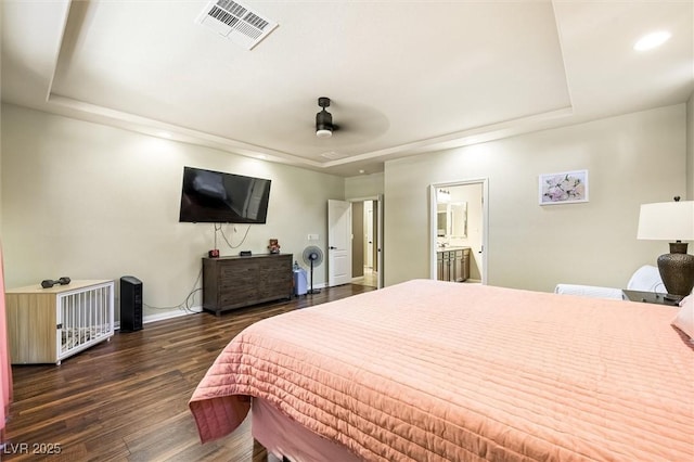 bedroom featuring a raised ceiling, dark hardwood / wood-style floors, ensuite bath, and ceiling fan