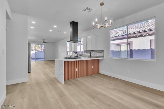 kitchen with kitchen peninsula, ceiling fan with notable chandelier, island range hood, light hardwood / wood-style flooring, and white cabinetry