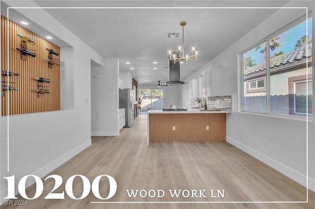 kitchen featuring white cabinetry, kitchen peninsula, stainless steel fridge, island exhaust hood, and a chandelier