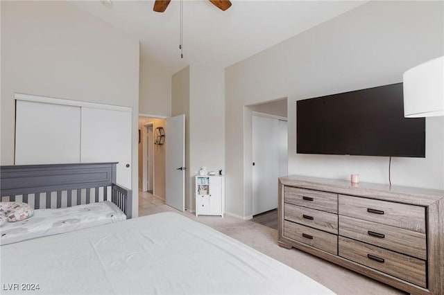 bedroom with ceiling fan, a closet, a towering ceiling, and light colored carpet