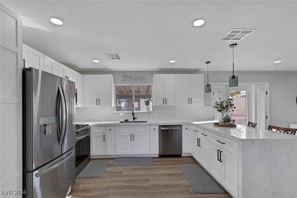 kitchen with sink, hanging light fixtures, light hardwood / wood-style flooring, white cabinetry, and stainless steel appliances