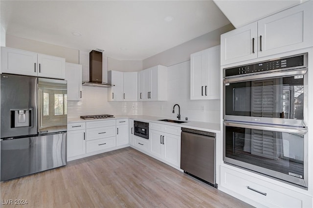 kitchen featuring white cabinetry, sink, black appliances, and wall chimney range hood