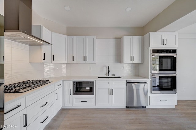 kitchen with white cabinets, sink, wall chimney exhaust hood, light wood-type flooring, and appliances with stainless steel finishes