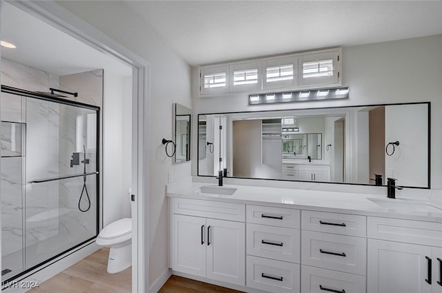 bathroom with hardwood / wood-style floors, vanity, toilet, and a shower with shower door