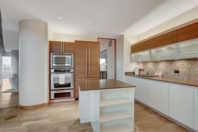 kitchen with stainless steel microwave, a center island, tasteful backsplash, white cabinets, and light wood-type flooring