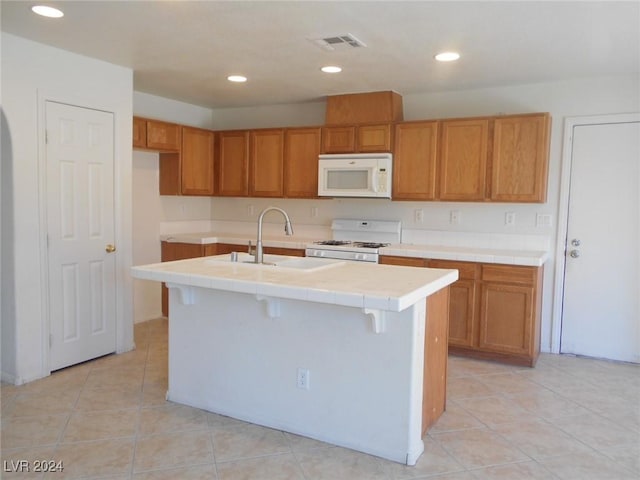 kitchen featuring light tile patterned flooring, white appliances, a center island with sink, and sink