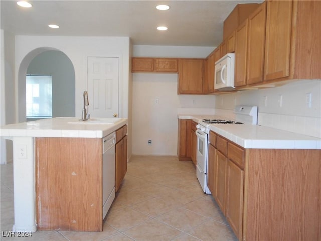 kitchen with white appliances, sink, tile countertops, an island with sink, and light tile patterned flooring