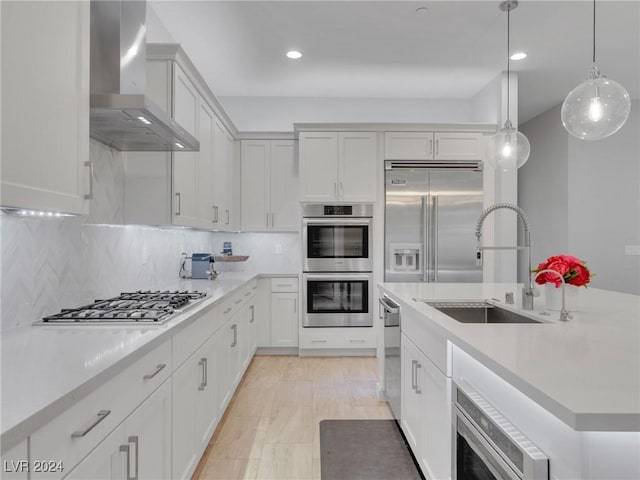 kitchen featuring wall chimney exhaust hood, sink, tasteful backsplash, hanging light fixtures, and appliances with stainless steel finishes