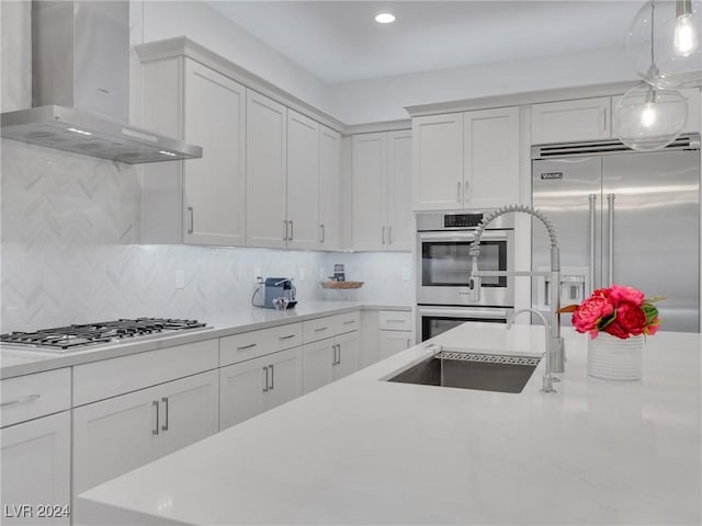 kitchen with appliances with stainless steel finishes, tasteful backsplash, sink, white cabinets, and wall chimney exhaust hood