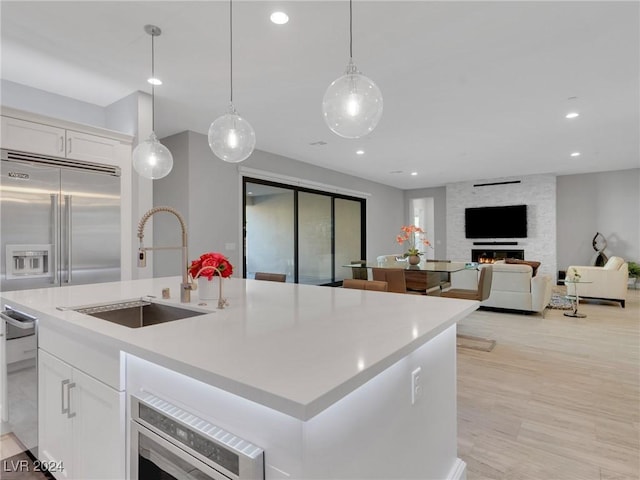 kitchen featuring sink, white cabinets, hanging light fixtures, stainless steel appliances, and a center island with sink