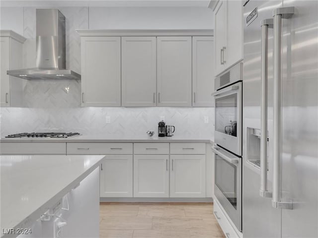 kitchen featuring backsplash, white cabinets, stainless steel appliances, and wall chimney range hood