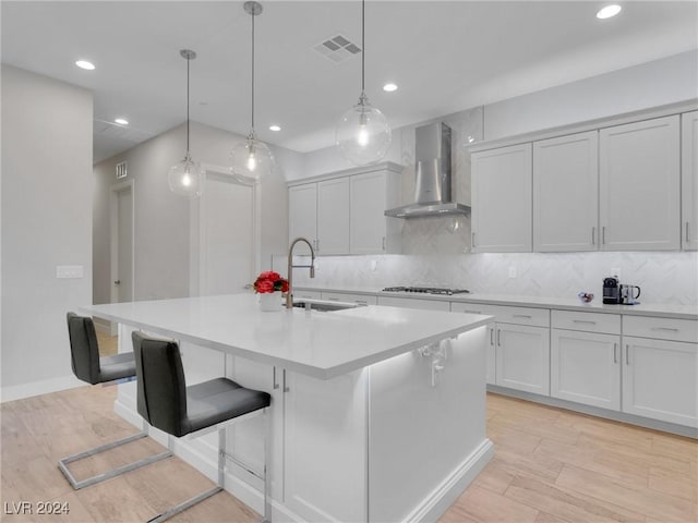 kitchen featuring wall chimney exhaust hood, a kitchen breakfast bar, hanging light fixtures, and a center island with sink