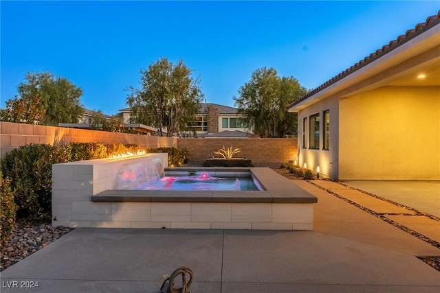 pool at dusk with a patio and an in ground hot tub