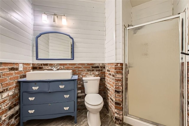 bathroom with an enclosed shower, vanity, toilet, and brick wall