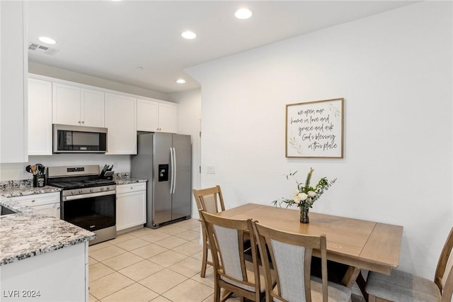 kitchen featuring light stone countertops, white cabinets, stainless steel appliances, and light tile patterned floors