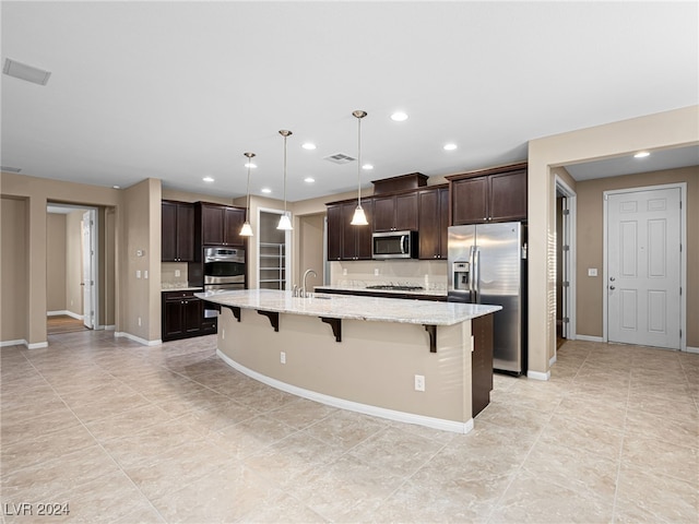 kitchen featuring a kitchen island with sink, a kitchen breakfast bar, decorative light fixtures, appliances with stainless steel finishes, and dark brown cabinets