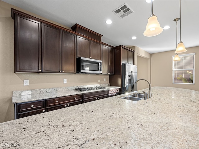 kitchen with light stone countertops, appliances with stainless steel finishes, dark brown cabinetry, sink, and decorative light fixtures