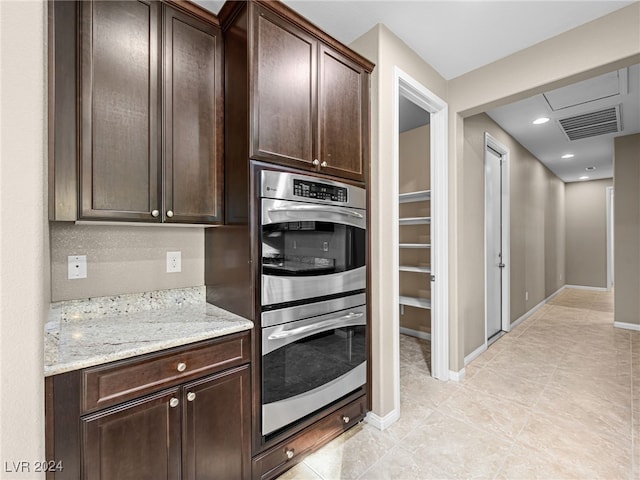 kitchen featuring light stone countertops, stainless steel double oven, dark brown cabinetry, and light tile patterned floors