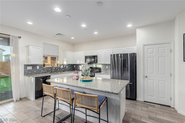 kitchen with a kitchen island, a sink, visible vents, white cabinets, and black appliances