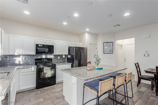 kitchen featuring a breakfast bar, visible vents, wood tiled floor, black appliances, and tasteful backsplash