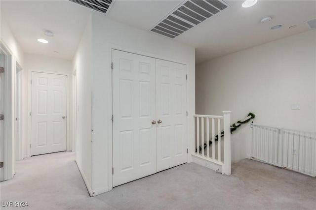 corridor with light carpet, radiator heating unit, visible vents, and an upstairs landing