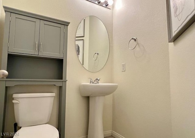 half bathroom featuring toilet, baseboards, and a sink