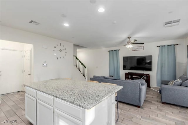 kitchen with a center island, visible vents, wood tiled floor, open floor plan, and white cabinetry