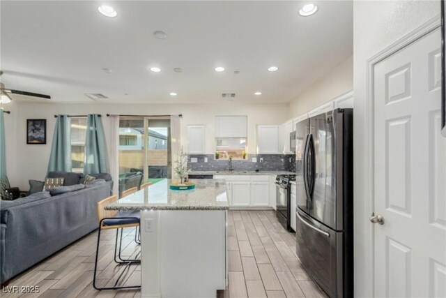 kitchen featuring open floor plan, freestanding refrigerator, black gas stove, a kitchen bar, and backsplash