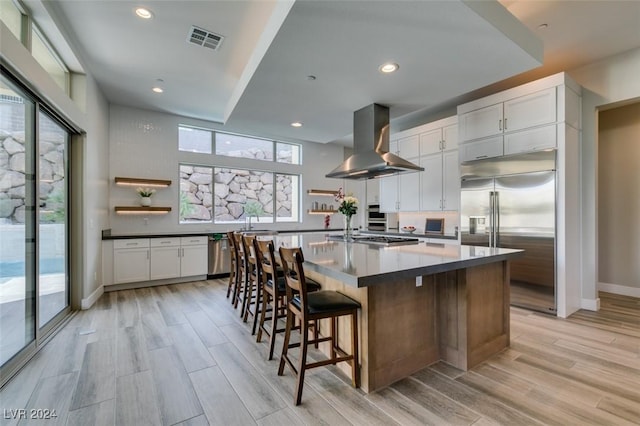 kitchen featuring exhaust hood, white cabinetry, stainless steel appliances, and a large island with sink