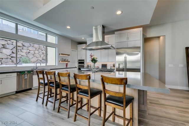 kitchen with white cabinetry, a center island, light hardwood / wood-style flooring, extractor fan, and appliances with stainless steel finishes