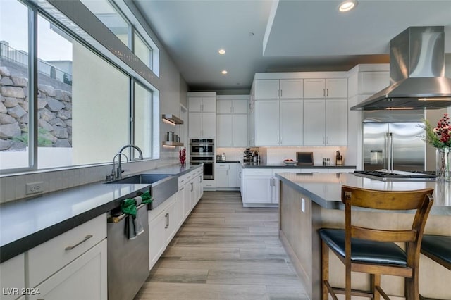 kitchen with wall chimney range hood, light hardwood / wood-style flooring, a breakfast bar, white cabinets, and appliances with stainless steel finishes