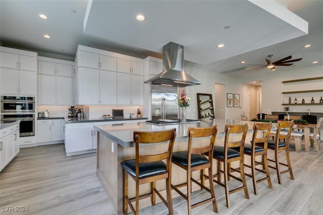 kitchen featuring appliances with stainless steel finishes, white cabinetry, a kitchen island with sink, and wall chimney range hood