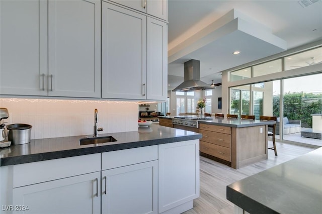 kitchen featuring sink, stainless steel gas stovetop, decorative backsplash, white cabinets, and island range hood