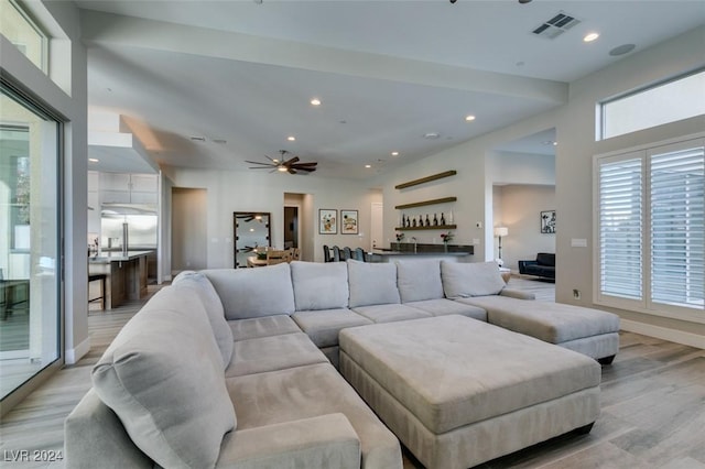 living room featuring bar area, light hardwood / wood-style floors, ceiling fan, and a healthy amount of sunlight