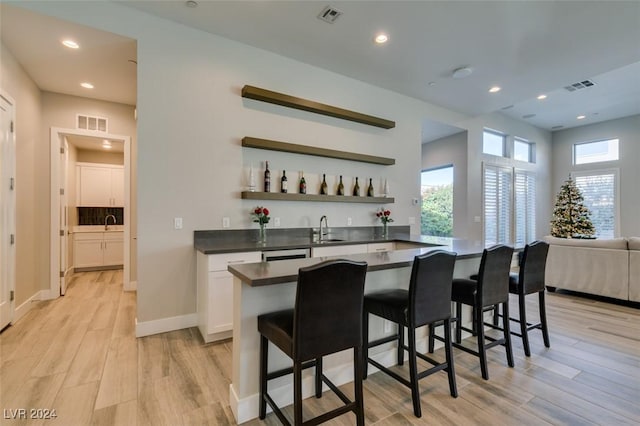 bar with sink, white cabinets, and light wood-type flooring