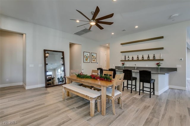 dining space with bar, ceiling fan, and light wood-type flooring