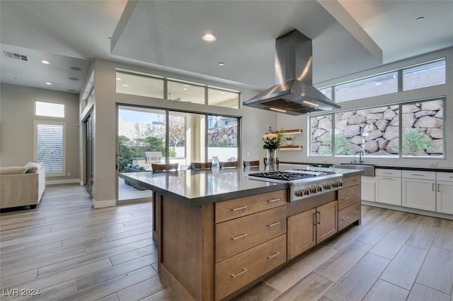 kitchen with a center island, light wood-type flooring, white cabinetry, island exhaust hood, and stainless steel gas cooktop