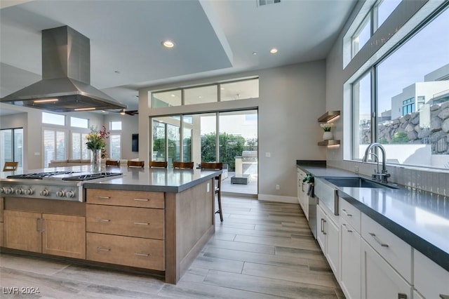 kitchen with sink, light hardwood / wood-style flooring, stainless steel gas stovetop, island range hood, and white cabinets