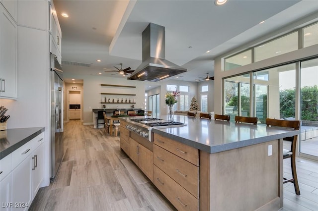 kitchen with a kitchen bar, island range hood, stainless steel appliances, white cabinetry, and a large island