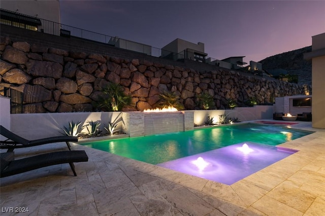 pool at dusk with a fireplace, a patio, and pool water feature