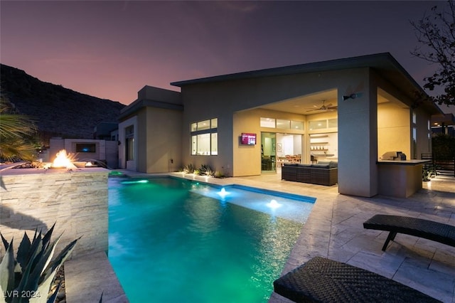 pool at dusk with outdoor lounge area, a patio area, and exterior kitchen