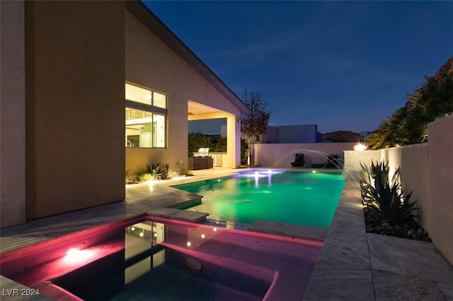 pool at night featuring pool water feature and a patio