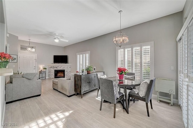 dining room with a fireplace, ceiling fan with notable chandelier, and light hardwood / wood-style floors