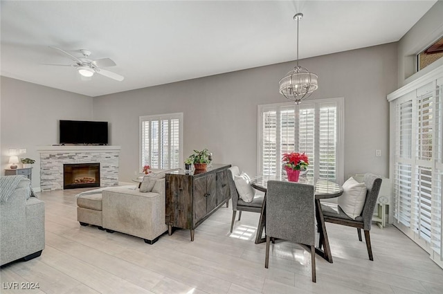 dining room featuring ceiling fan with notable chandelier, a healthy amount of sunlight, light wood-type flooring, and a tile fireplace